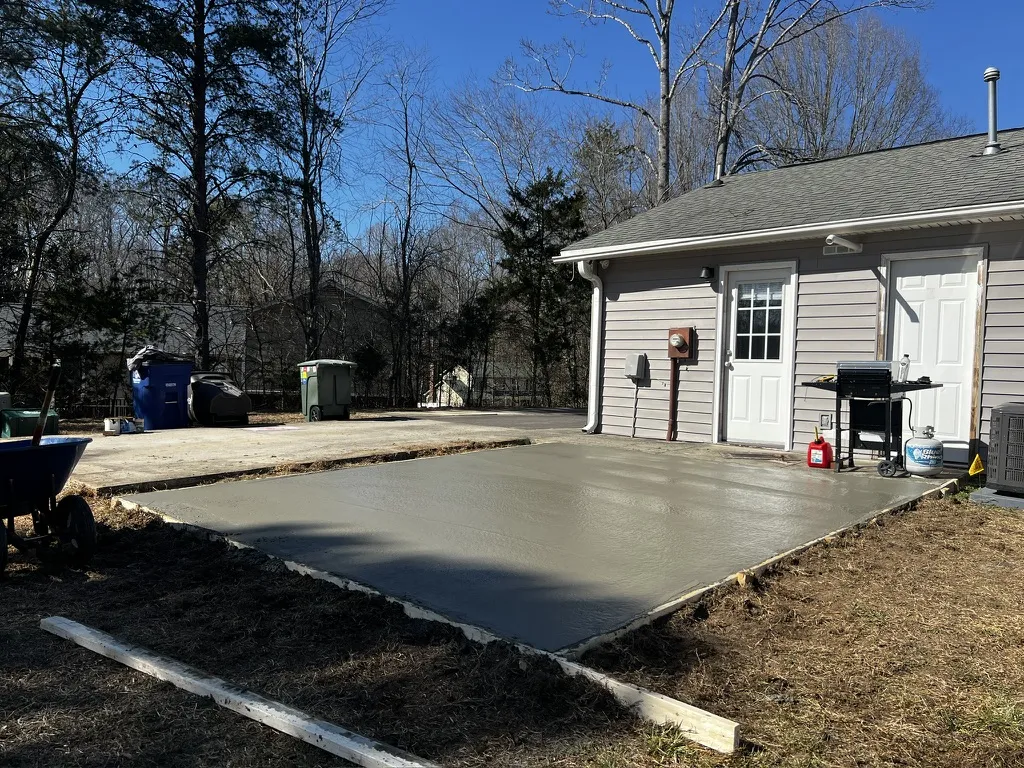 New concrete patio beside a backyard outbuilding